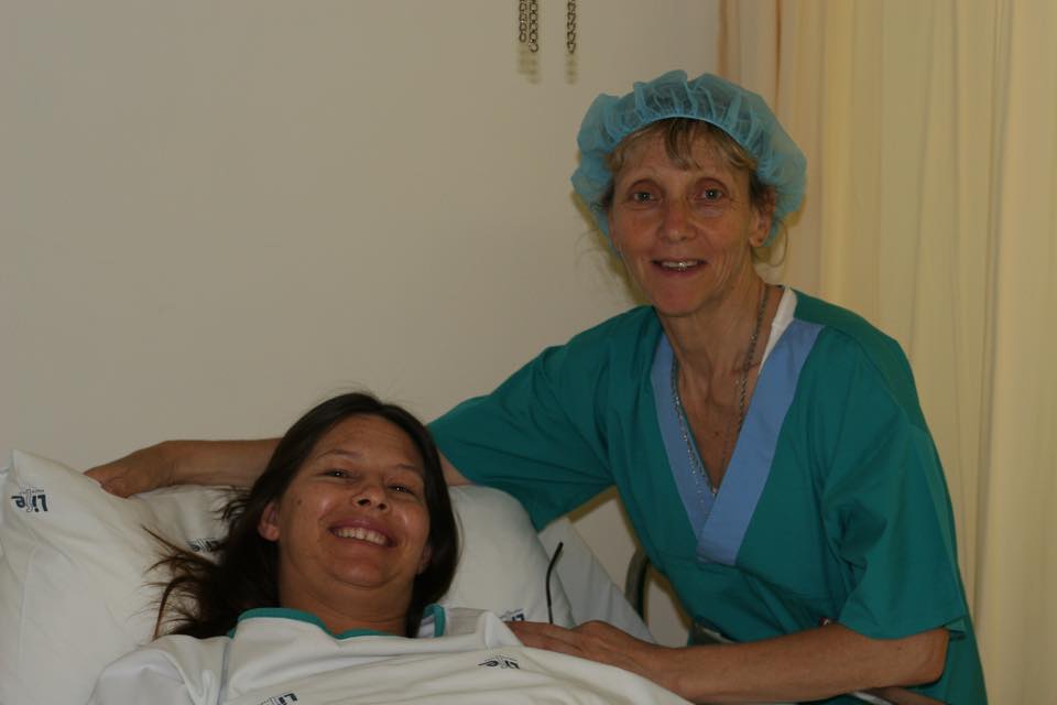 A WOMBS doula in theatre scrubs beside a smiling mother in hospital